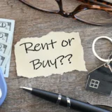 Nota con la pregunta “Rent or Buy?” junto a una calculadora, dinero y llaves de vivienda