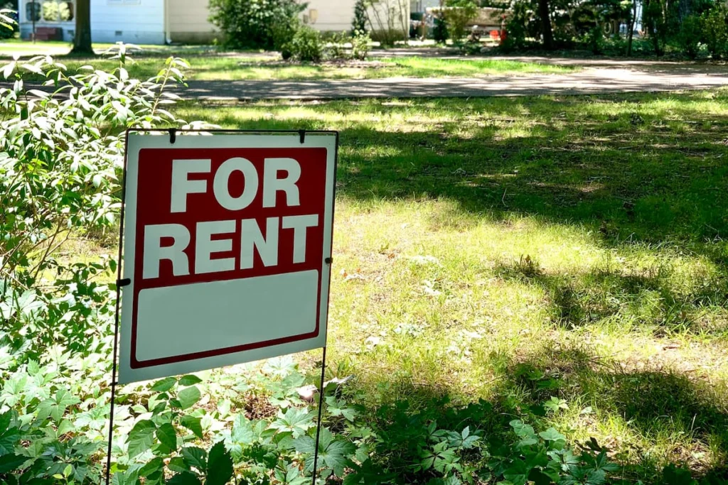 Cartel de “For Rent” colocado sobre el césped frente a una vivienda en una zona residencial