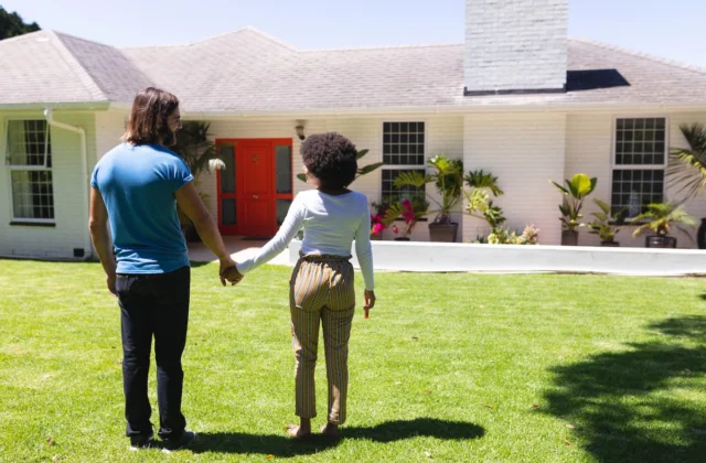 Pareja tomada de la mano frente a una casa unifamiliar con jardín en una zona residencial de Florida