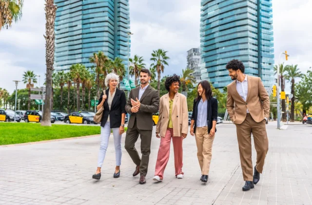 Grupo de profesionales caminando por una zona urbana con edificios modernos y palmeras