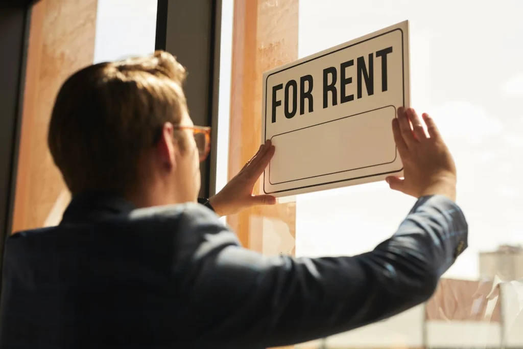 Persona colocando un cartel de “For Rent” en la ventana de una propiedad disponible para alquiler