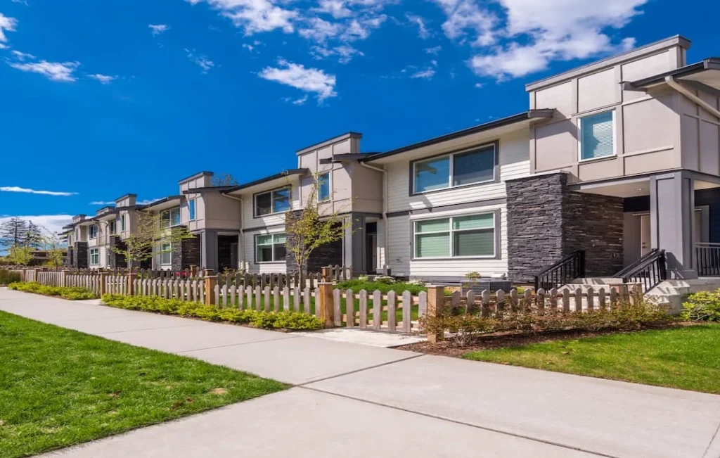 Hilera de townhouses de dos plantas con fachadas de piedra y acera arbolada en un día soleado