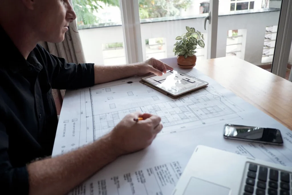 Hombre revisando planos arquitectónicos de una vivienda junto a una tableta con el mismo plano
