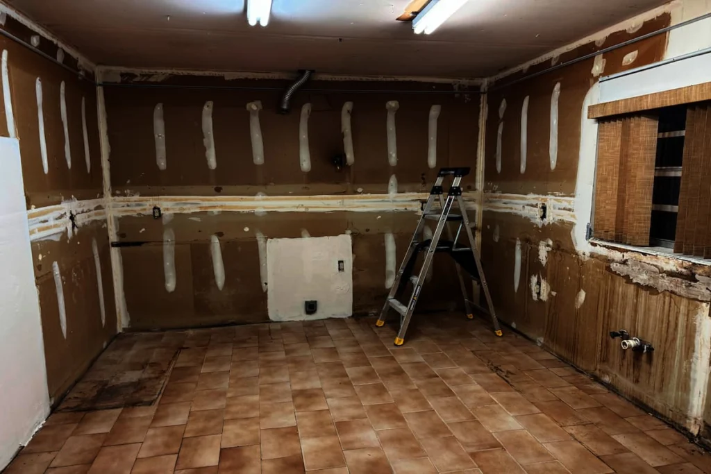 Espacio de cocina durante la demolición, con gabinetes retirados, paredes expuestas y una escalera de trabajo