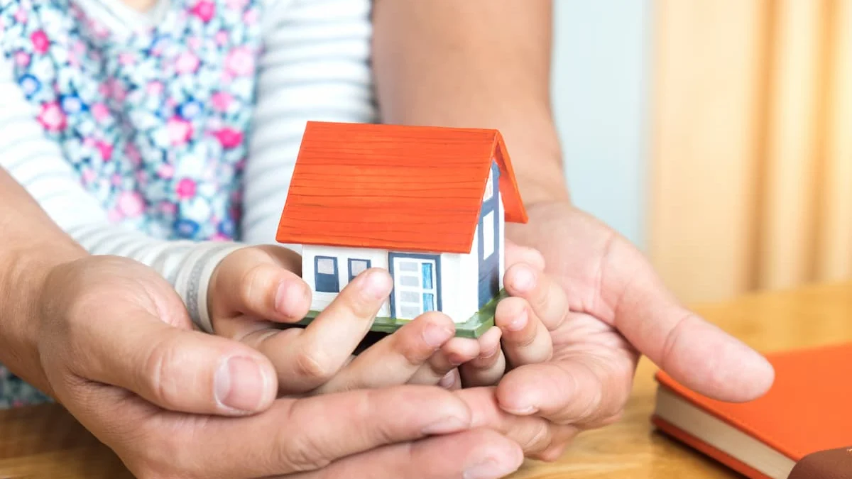 Manos de un adulto y un niño sosteniendo juntos una pequeña casa, como símbolo de vivienda, familia y patrimonio