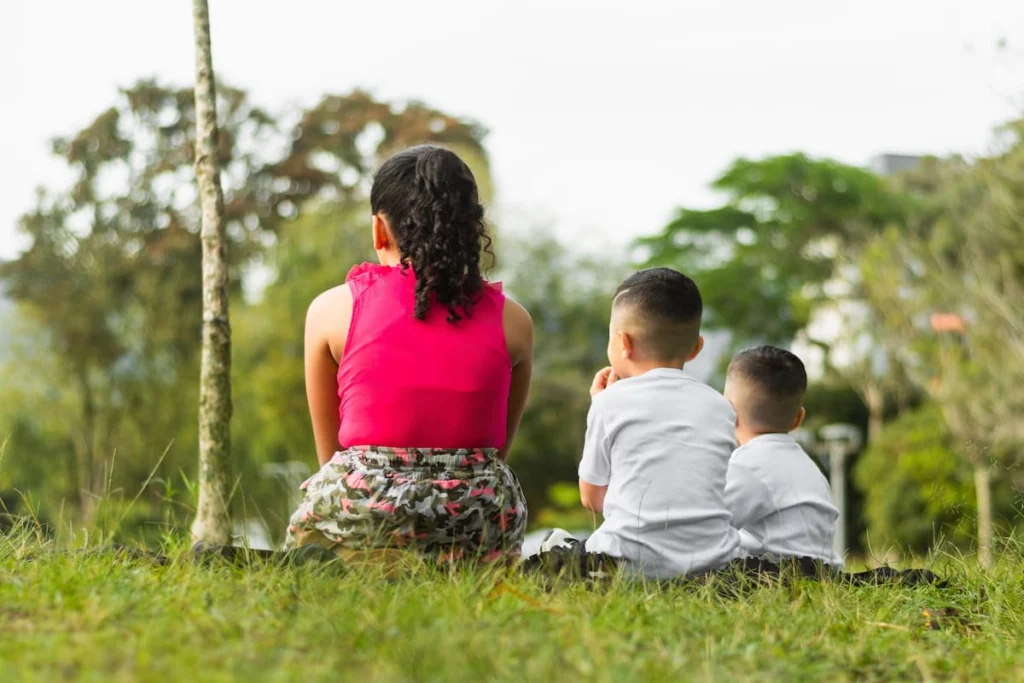 Mujer con dos niños sentados sobre el césped en un entorno verde y residencial