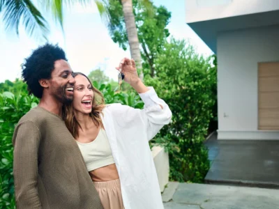 Pareja sonriente mostrando las llaves de su nueva casa frente a la entrada de una vivienda