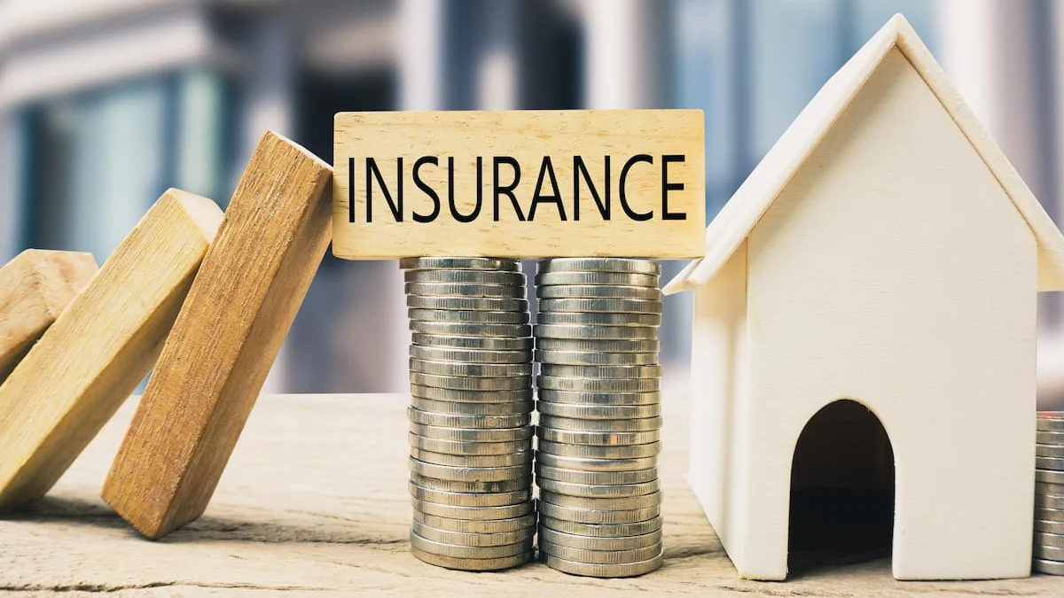 Modelo de casa junto a monedas apiladas y un bloque con la palabra insurance.
