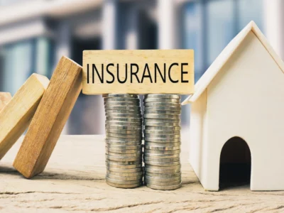 Modelo de casa junto a monedas apiladas y un bloque con la palabra insurance.