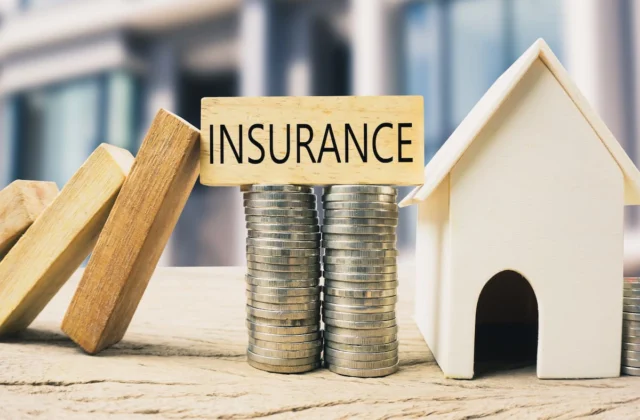 Modelo de casa junto a monedas apiladas y un bloque con la palabra insurance.