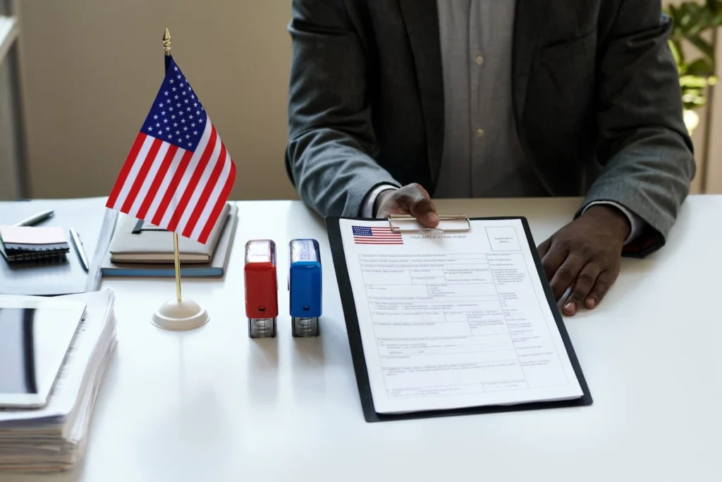 Profesional revisando un formulario de solicitud de visa junto a una bandera de Estados Unidos y sellos de oficina
