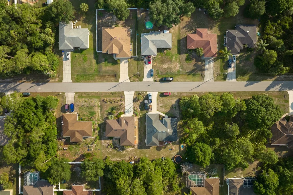 Vista aérea de un barrio residencial con casas unifamiliares, jardines, entradas de vehículos y abundante vegetación