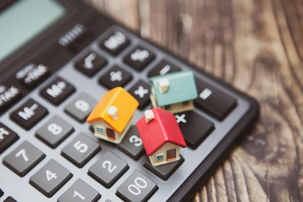 Tres pequeñas maquetas de viviendas colocadas sobre una calculadora, en referencia al cálculo de costos y valores inmobiliarios.