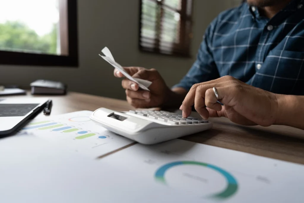 Persona utiliza una calculadora mientras revisa recibos y gráficos financieros sobre una mesa de trabajo.
