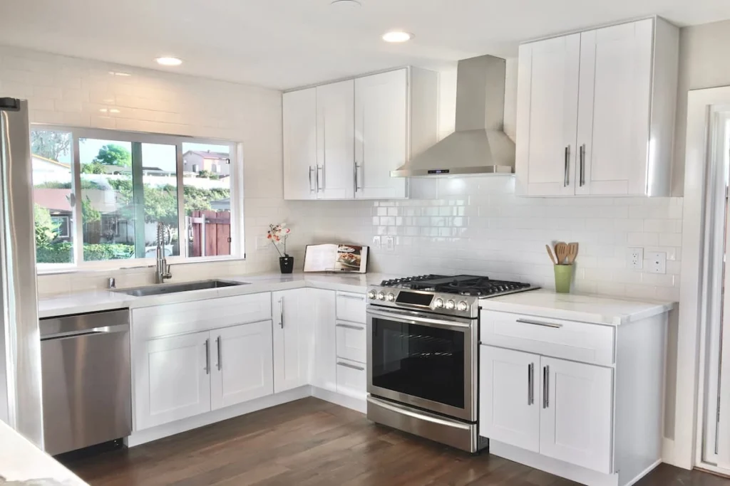 Cocina moderna con gabinetes blancos, encimeras claras, electrodomésticos de acero inoxidable y revestimiento de azulejos blancos.