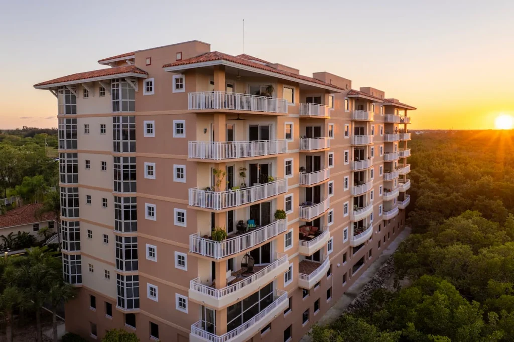Edificio residencial de varios pisos con balcones amplios, rodeado de vegetación y fotografiado durante el atardecer.