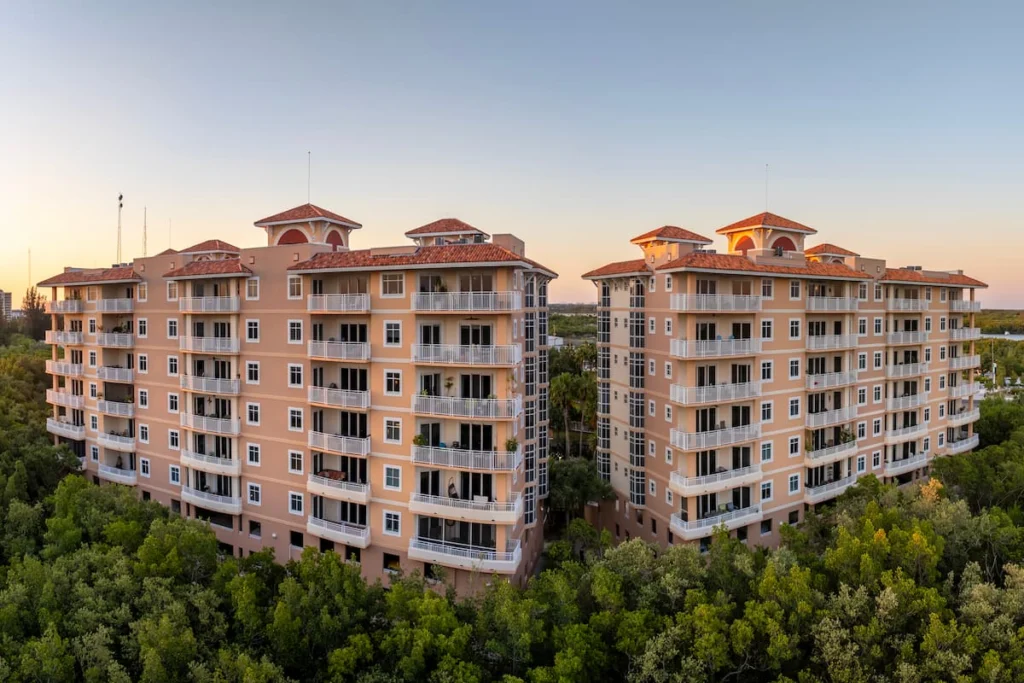 Dos edificios residenciales de varios pisos con balcones amplios, rodeados de abundante vegetación.