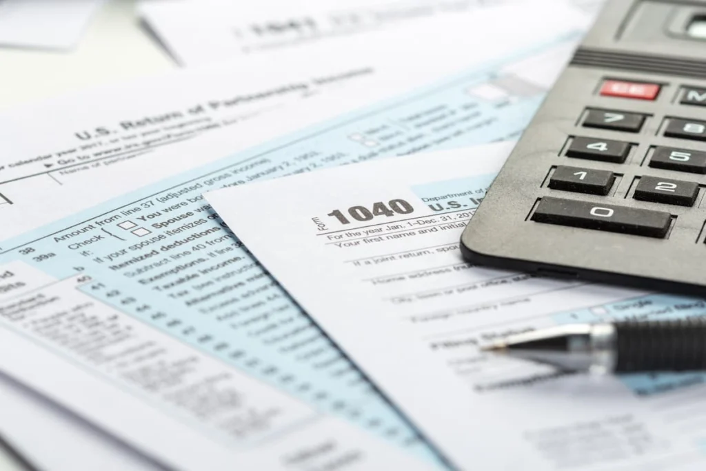 Formularios de impuestos de Estados Unidos junto a una calculadora y un bolígrafo sobre una mesa.