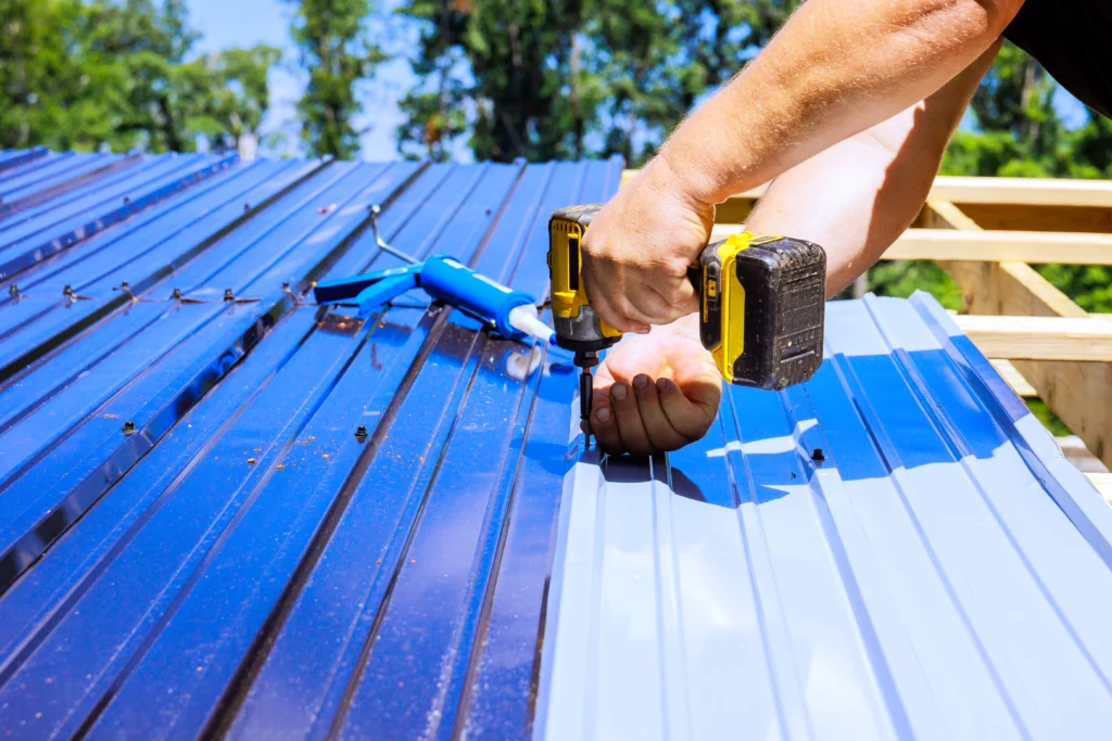 Trabajador fija una lámina metálica azul sobre la estructura de un techo utilizando un taladro eléctrico.