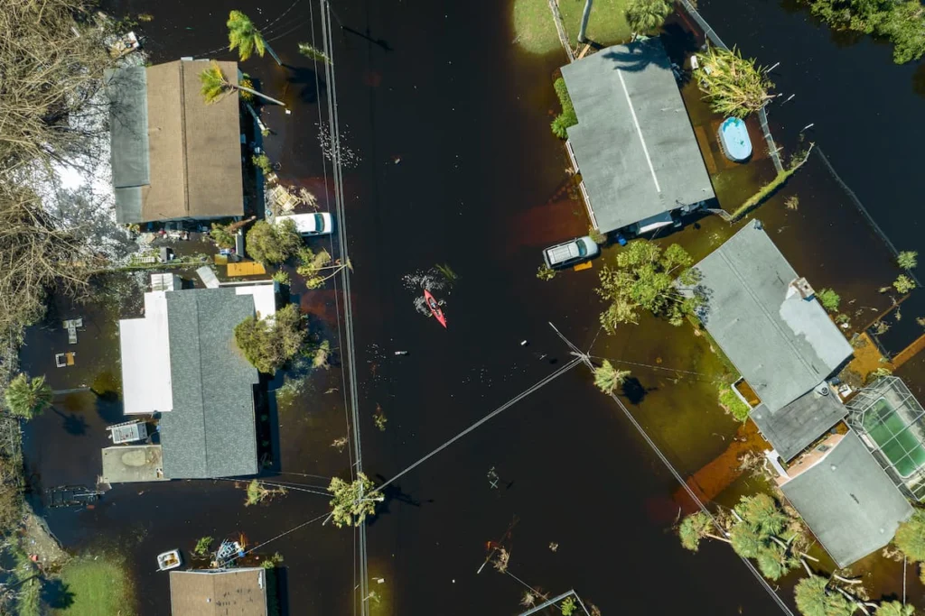 Vista aérea de una zona residencial inundada, con viviendas rodeadas por agua y una persona desplazándose en una pequeña embarcación.