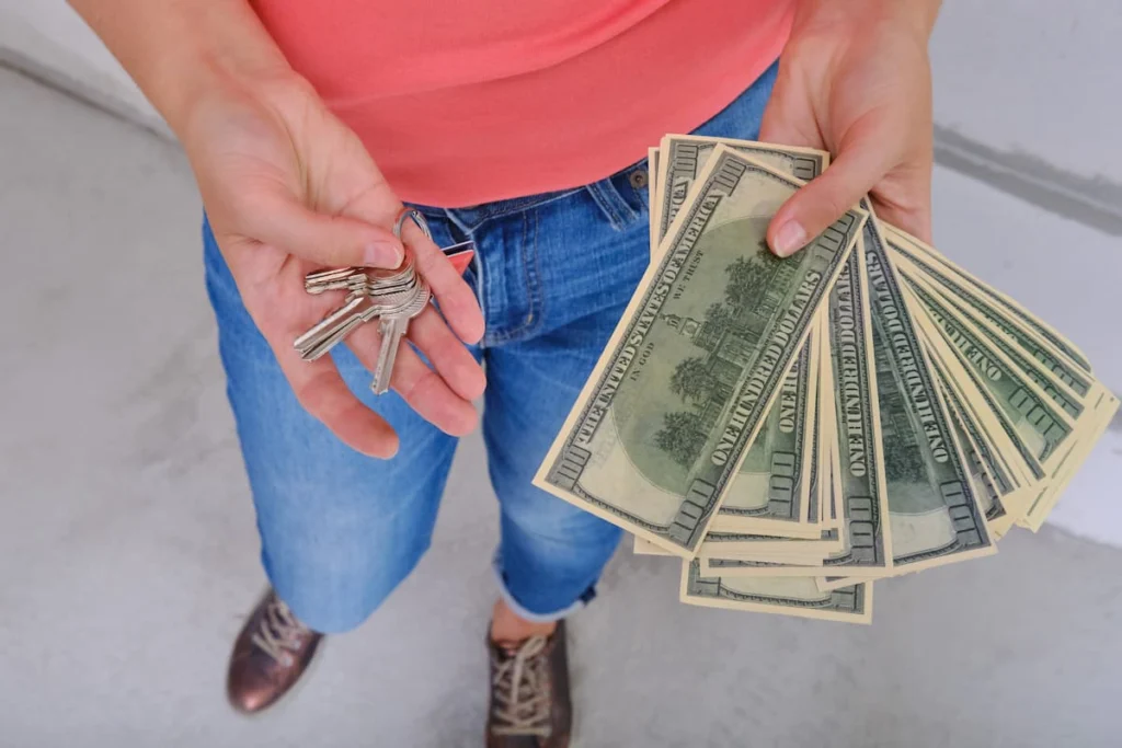 Persona sostiene un juego de llaves en una mano y varios billetes de cien dólares en la otra.