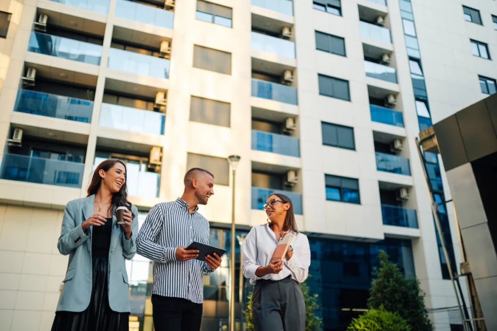 Tres profesionales conversan frente a un edificio residencial de varios pisos con balcones de vidrio.