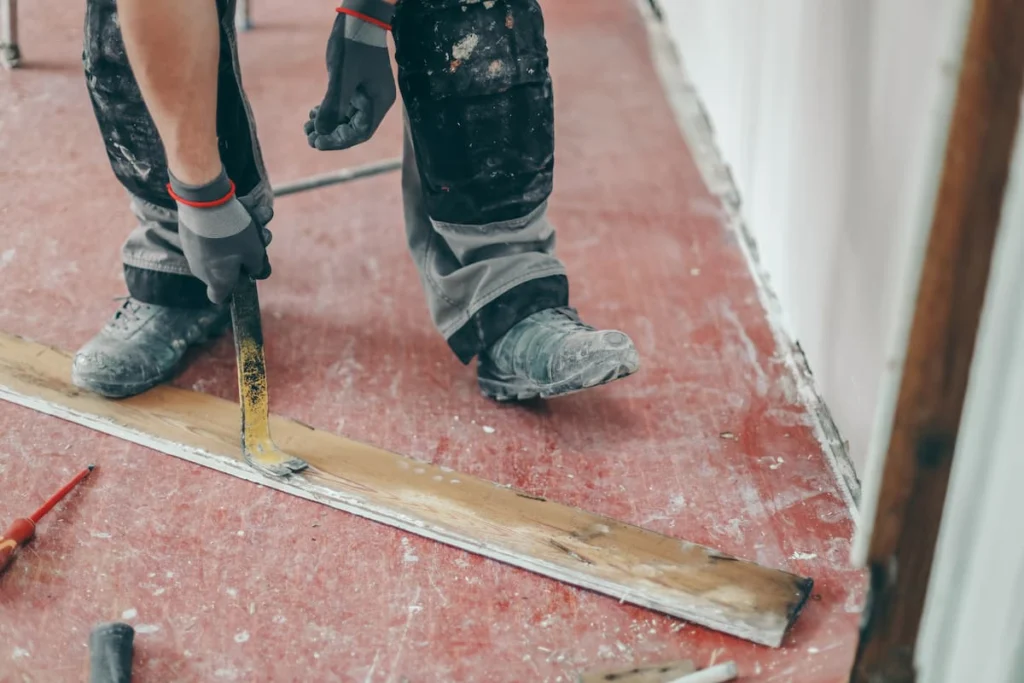 Trabajador retira una moldura de madera del suelo con una palanca durante una obra de remodelación interior.