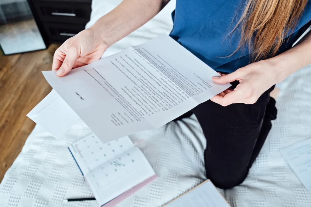 Mujer revisa un documento impreso mientras está sentada junto a varios papeles y una libreta.