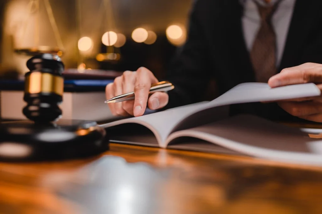 Profesional revisa documentos legales con un bolígrafo junto a un mazo judicial sobre una mesa.