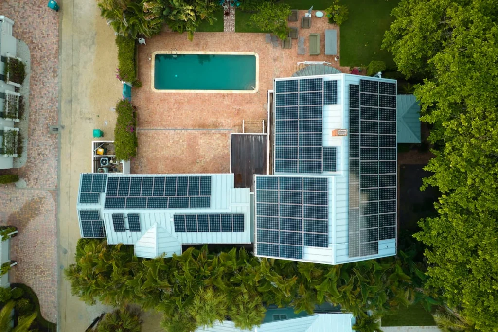 Vista aérea de una vivienda con numerosos paneles solares instalados sobre el techo, junto a una piscina y áreas verdes.